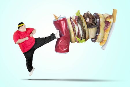 Picture of young fat man wearing sportswear while kicking soft drink and fast foodの写真素材