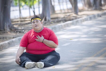 Picture of overweight man having heart pain after exercising while sitting in the parkの写真素材