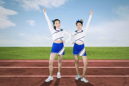 Picture of two cheerleaders lifting hand while cheering at the football field