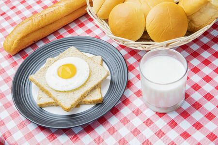 Top view of fried egg on whole grain toast with a glass of milk and assorted fresh breads for...