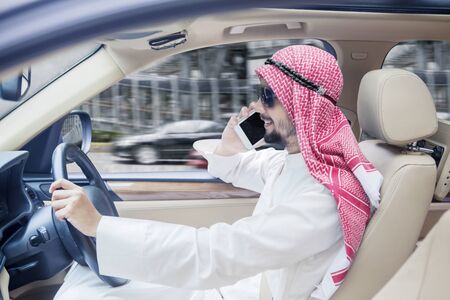Picture of Arabian businessman driving a car while talking on a mobile phoneの写真素材