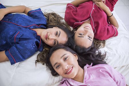 Top view of teenage girls smiling at the camera while lying on the bed. Shot at homeの写真素材