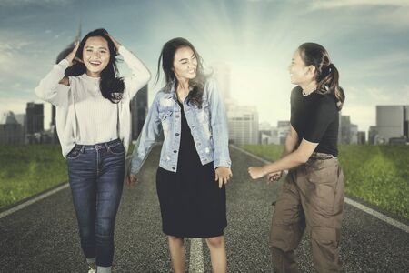 Picture of three teenagers looks happy while walking together on the road with sunlight backgroundの写真素材
