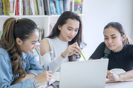 Group of female college students using a laptop while studying together in the library the library