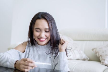 Picture of teenage girl looks happy while holding a pregnancy test while sitting in the living room
