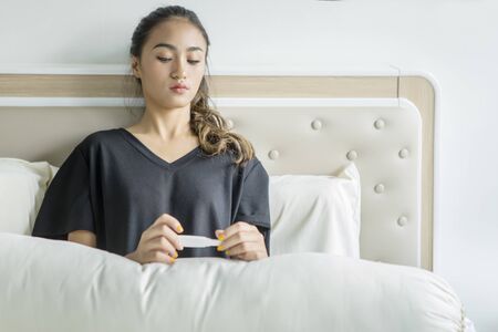 Frustrated teenage girl holding a pregnancy test result while sitting in the bed