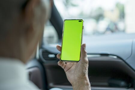 Back view of unknown old man using a mobile phone with blank green screen while sitting inside the carの写真素材