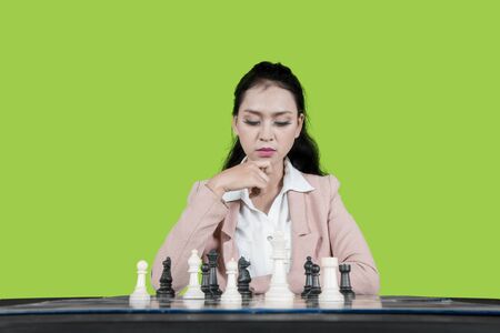 Pensive businesswoman thinking about chess game strategies while sitting in the studio with green screen backgroundの写真素材
