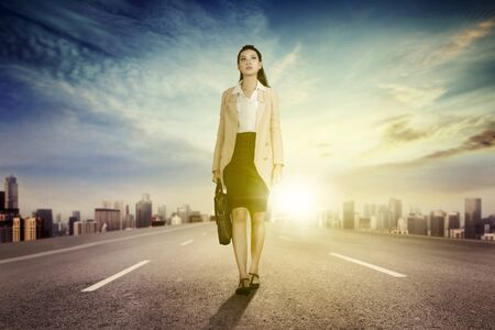 Low angle view of a beautiful female entrepreneur carrying a briefcase while walking on the road with skyscraper backgroundの写真素材