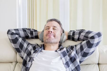 Young man enjoying music with headphones in the living room while relaxing on the sofa at homeの写真素材