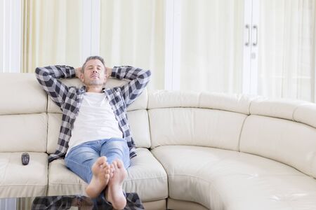 Portrait of a Caucasian man resting on the sofa while watching TV in the living room. Shot at homeの写真素材