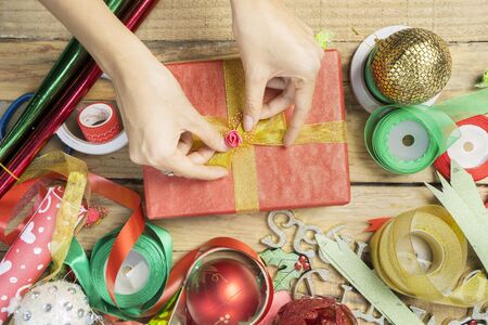 Hands of unknown female decorating a Christmas gift with ribbon on the wooden tableの写真素材
