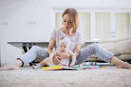 Caucasian mother and her baby girl playing together while sitting on the carpet in the living room....