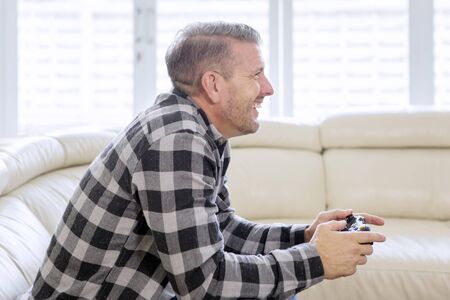 Side view of Caucasian man using joystick while playing video games and sitting on the sofa at home