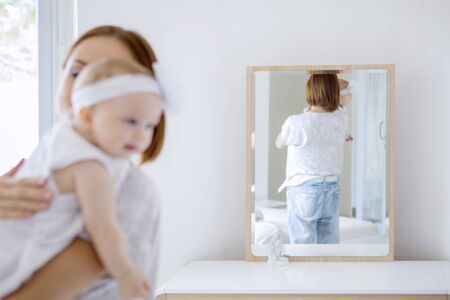 Reflection of rear view of a young mother holding her baby while standing in front of the mirror in the bedroom. Shot at homeの写真素材