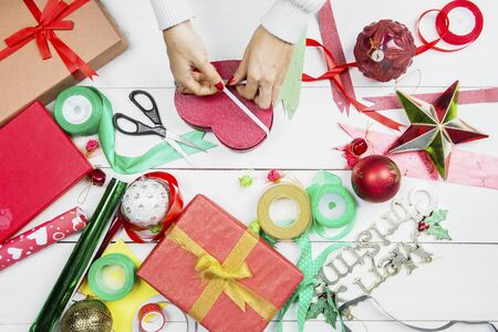 Top down view of unknown woman hands decorating Christmas gift shaped heart symbol with ribbonの写真素材