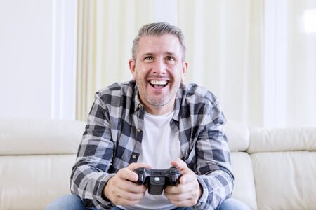Cheerful man using joystick while playing video games and sitting on the sofa at home