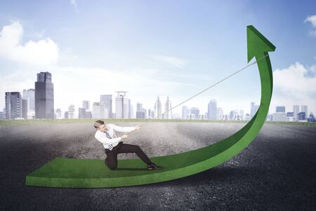 Caucasian businessman using a chain to pull an upward arrow at outdoors with misty city background