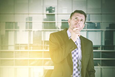 Caucasian businessman thinking an idea while holding his chin and standing near the window in the officeの写真素材
