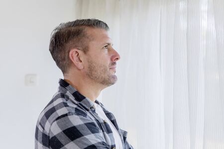 Side view of Caucasian man thinking something while standing near the windowの写真素材