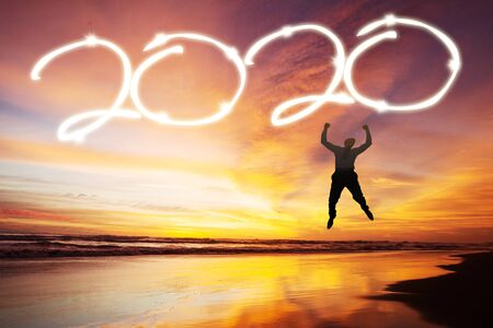 Silhouette of young businessman jumping on the beach with number 2020 in the sky at sunrise