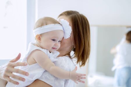 Close up of cute baby girl looks happy while embraced by her mother at homeの写真素材