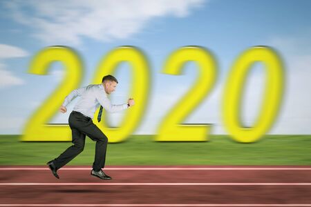 Side view of Caucasian businessman sprinting on the track line with blurred number 2020 background