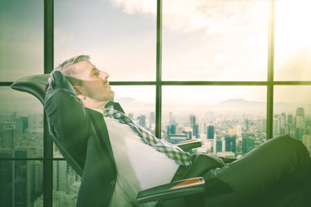 Caucasian young man at the office sitting and leaning back daydreaming on a chairの写真素材