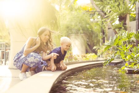 Caucasian mother and her son looks happy while playing in the fountain at summer timeの写真素材