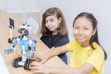 Two cute little girls smiling at the camera while constructing a bricks robot together in the...