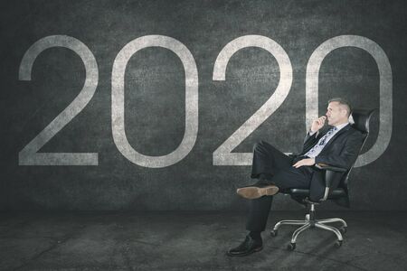 Side view of young businessman thinking of resolution next to 2020 background while sitting on a...