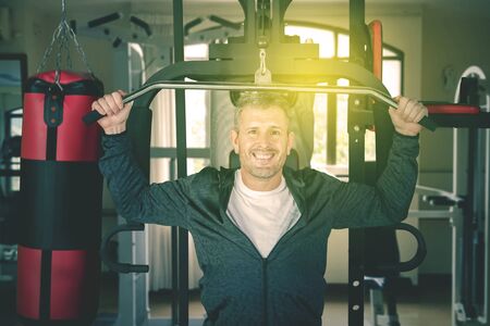Portrait of caucasian man exercising a weight lifting while smiling on camera at the gym centerの写真素材