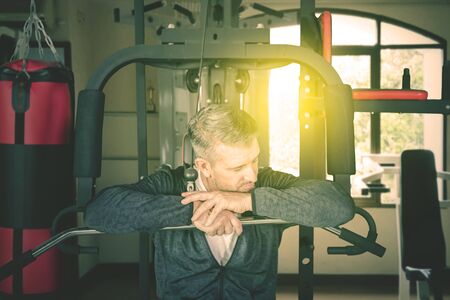Close up of Caucasian man resting on the exercise machine while exercising in the gym center at dusk...