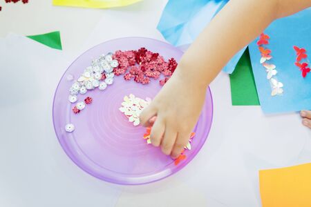 Hands of a preschool girl gluing colorful butterfly on a blue paper while studying in the...