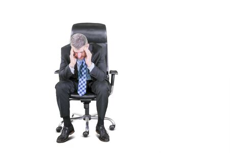 Caucasian businessman in formal suit sitting on armchair and holding his head in depression, isolated on whiteの写真素材