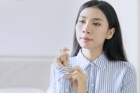 Attractive Asian businesswoman buttoning long sleeve shirt getting ready for workの写真素材