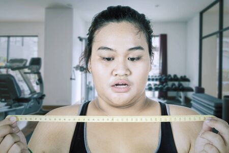 Fat Asian woman wearing sportswear while feeling shocked after seeing her body checkup in the gym centerの写真素材