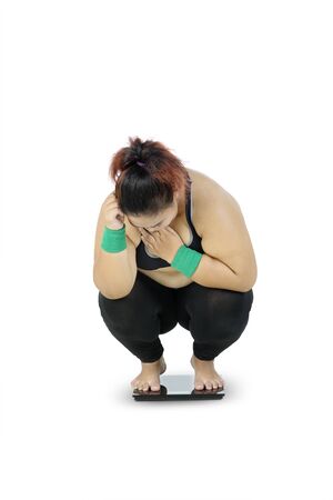 Unidentified fat woman wearing sportswear while squatting down to her knees due to her increasing body weight, isolated in white backgroundの写真素材