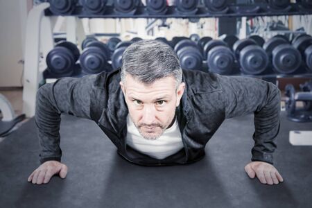 Middle aged caucasian man doing push-ups in weight room
