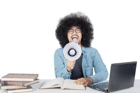 Male student with big afro hair screaming on megaphone while studying isolated over white backgroundの写真素材