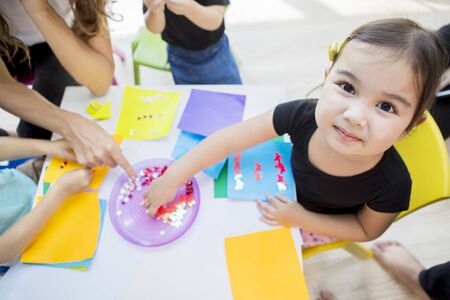 Closeup of a pupil making origami stickers while smiling to the camera in the classroomの写真素材
