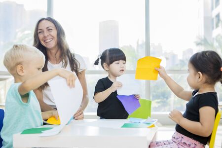 Beautiful teacher laughing happily while her adorable pupils creating frenzy in the classroomの写真素材