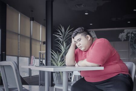 Fat Asian man sitting on a chair while daydreaming somberly in a cafe