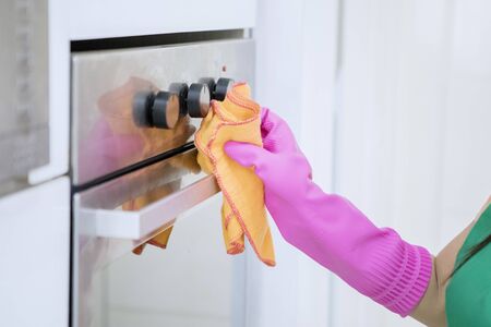 Closeup of right hand belongs to a woman wiping and cleaning an oven in the kitchen