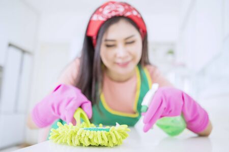 Focused portrait of beautiful Asian woman wiping and cleaning the table with a smile in her houseの写真素材