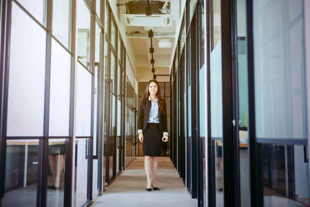 Beautiful Asian businesswoman wearing suit while smiling at camera seriously on the office hallwayの写真素材