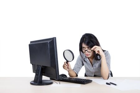 Portrait of beautiful Asian businesswoman wearing formal attire while inspecting a file on her desktop with a magnifying glass, isolated in white backgroundの写真素材