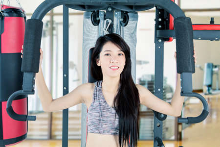 Portrait of beautiful Asian woman smiling at camera while using a gym equipment in the gym center
