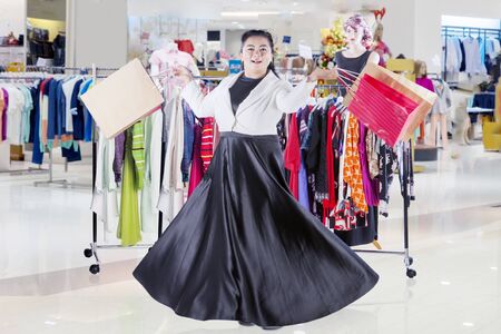 Fat Asian woman looking at camera while dancing happily and joyfully in a clothing storeの写真素材