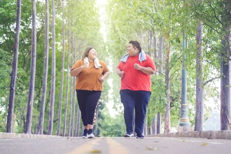 Fat Asian couple chatting happily & joyfully while jogging on the road at the parkの写真素材